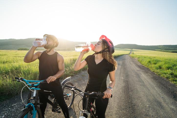 man and woman outside on bicycles drinking water