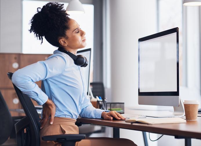 woman at desk touching her back