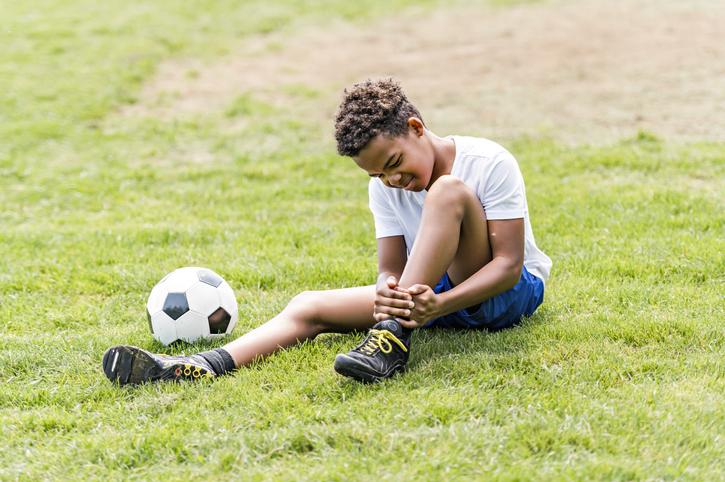 young boy holding ankle outside next to soccer ball