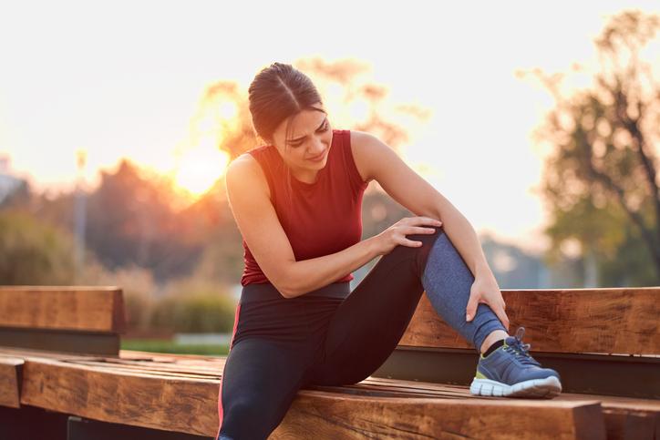 woman outside holding leg and knee on bench