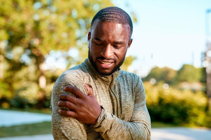 man outside touching shoulder