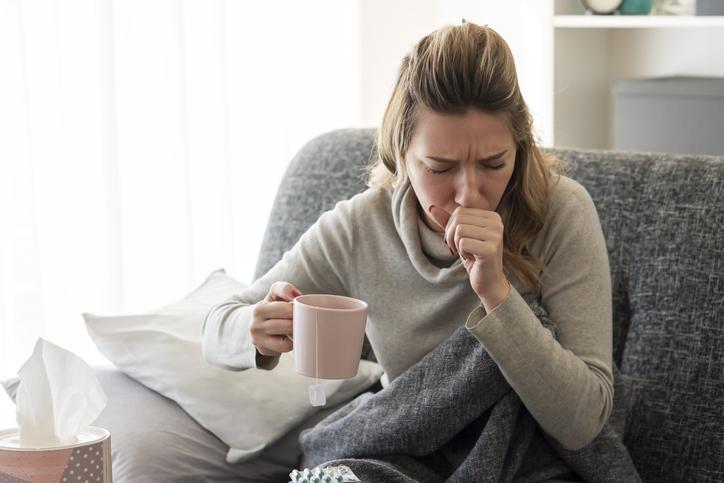 woman coughing on couch, holding mug