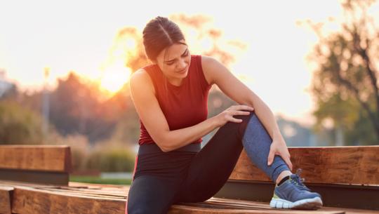 woman outside holding leg and knee on bench