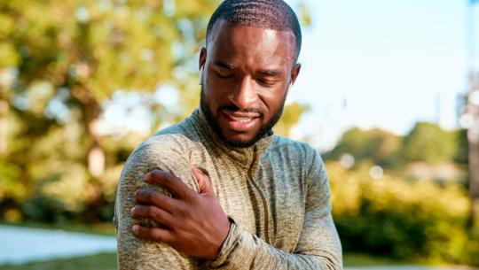 man outside touching shoulder