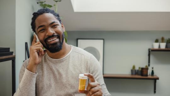 man on phone holding pill bottle