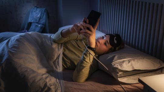 young woman looking at cell phone in bed