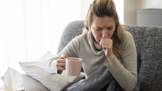 woman coughing on couch, holding mug