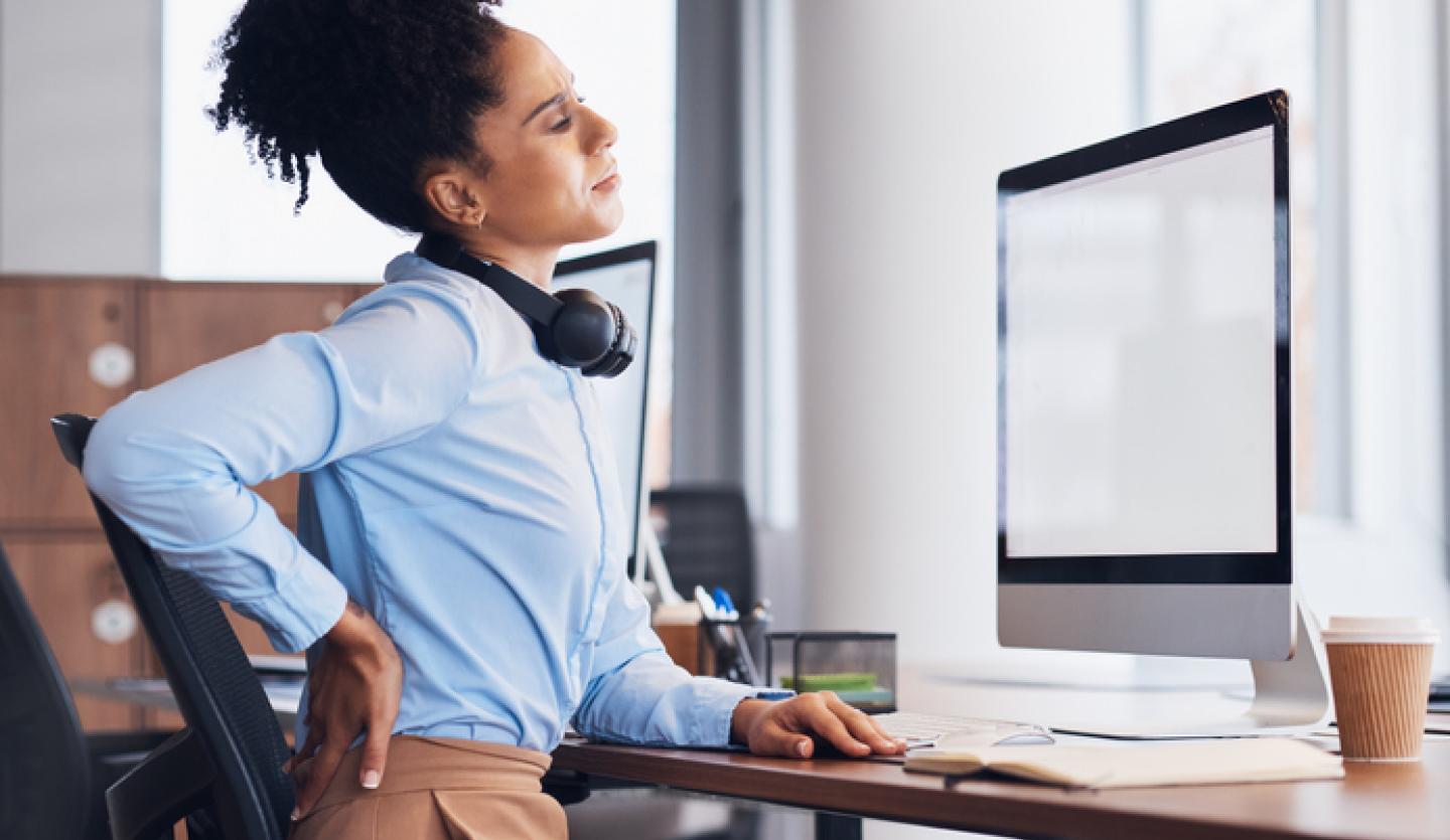 woman at desk touching her back