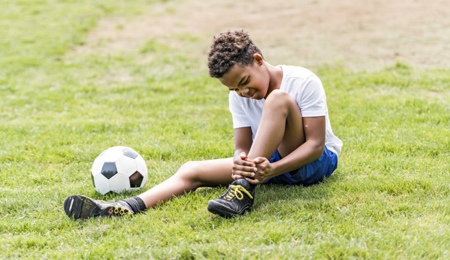 young boy holding ankle outside next to soccer ball