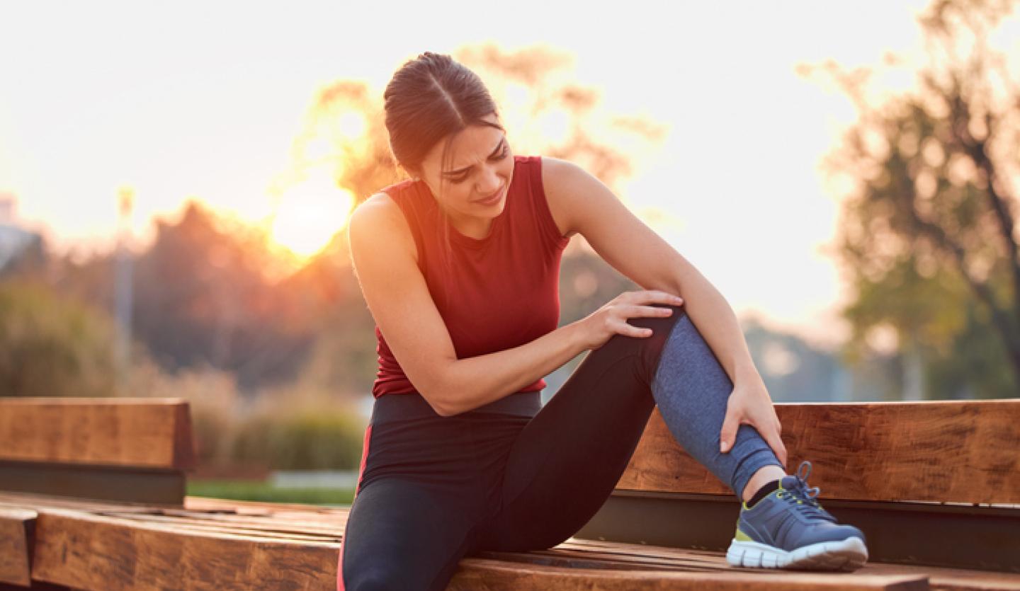 woman outside holding leg and knee on bench