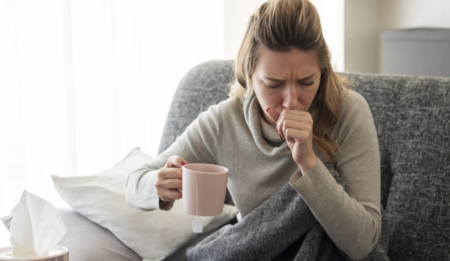 woman coughing on couch, holding mug