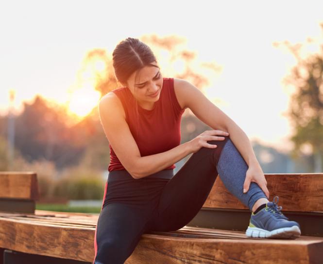 woman outside holding leg and knee on bench
