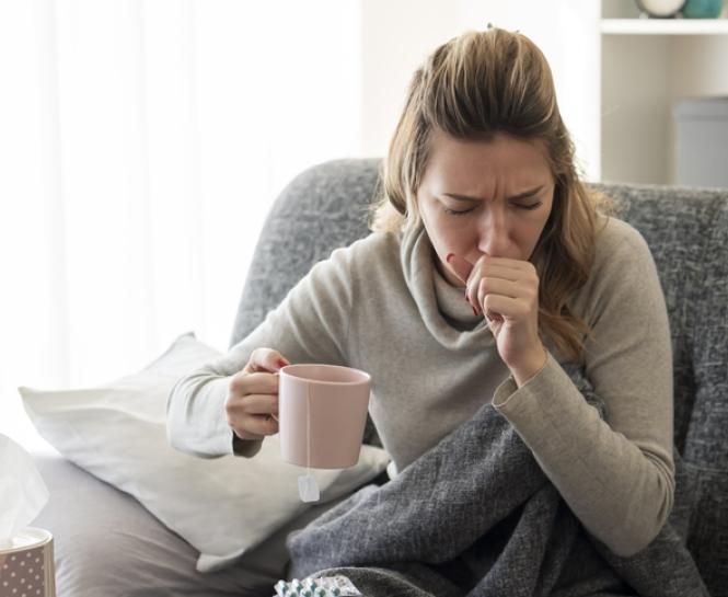 woman coughing on couch, holding mug