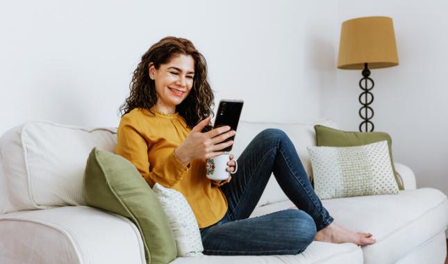 woman on couch holding mug and looking at phone