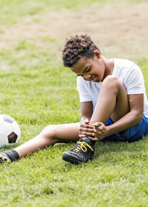 young boy holding ankle outside next to soccer ball